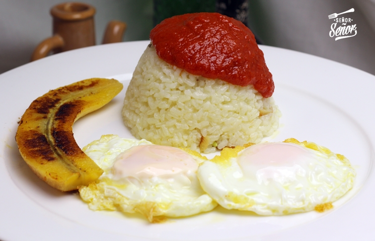 a mound of rice with ketchup on top, two halves of a fried banana and a fried egg