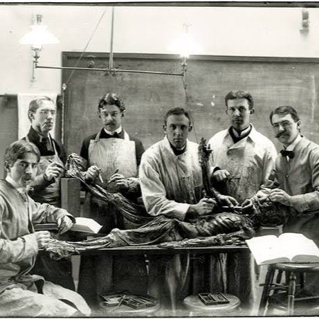 Old photo of anatomists around a cadaver. One is smoking.